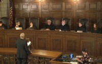 From left: Justice Jonathan Papik, Justice Stephanie Stacy, Justice Lindsey Miller-Lerman, Judge Timothy Burns, Justice William Cassel, Justice Jeff Funke, and Judge Shelly Stratman. Arguing before the Court is attorney James D. Smith. Recording Court arguments is Allyson Stewart. (Nebraska Public Media)